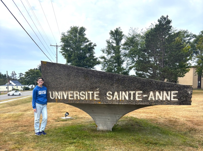 Un étudiant près du panneau de l'Université Sainte-Anne